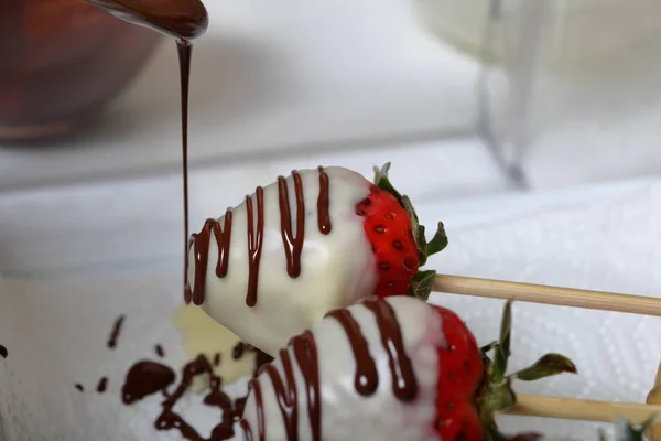Strawberries glazed in black and white chocolate dries on a plate. On the work surface visible drops of chocolate. Cooking strawberries glazed in chocolate. — Stock Photo, Image