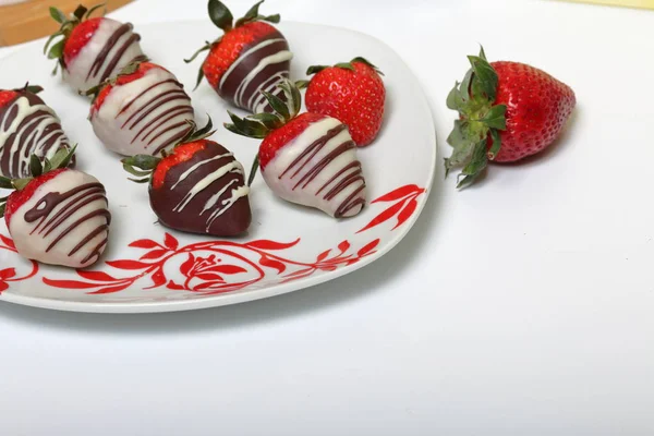 Erdbeeren glasiert in schwarzer und weißer Schokolade. auf einem weißen Teller mit Muster liegen. — Stockfoto