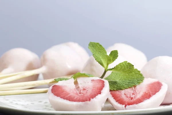 Aardbeien in yoghurt. Bessen zijn gekleed op houten spiesjes en ondergedompeld in yoghurt. In de buurt zijn twee helften van het dessert. Zichtbare rode sappige aardbei vlees. Versierd met muntblaadjes. — Stockfoto
