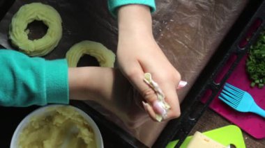 Bir kadın fırın çarşafında patates püresi halkaları oluşturur. Pasta çantası yardımıyla. Yemek pişirme için diğer malzemelerin yanında.