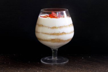 Cam kadehteki tatlı. Katmanlar bisküvi kırıntıları ve krem koydu. Çilek dilimleri ile dekore edilmiştir. Ceviz ilavesi ile. Karanlık bir arka planda.