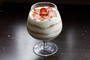 Cam kadehteki tatlı. Katmanlar bisküvi kırıntıları ve krem koydu. Çilek dilimleri ile dekore edilmiştir. Ceviz ilavesi ile. Karanlık bir arka planda.