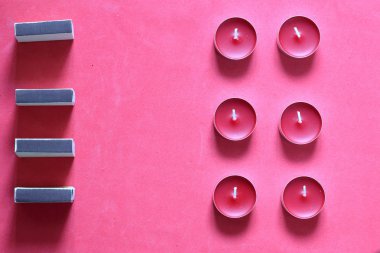 Bir satırda düzenlenmiş Dekoratif mumlar ve kibrit kutuları. Pembe bir arka planda.
