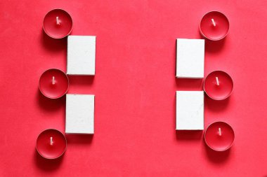 Bir satırda düzenlenmiş Dekoratif mumlar ve kibrit kutuları. Pembe bir arka planda.