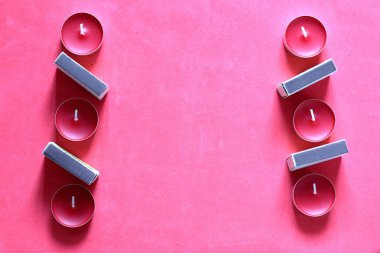 Bir satırda düzenlenmiş Dekoratif mumlar ve kibrit kutuları. Pembe bir arka planda.