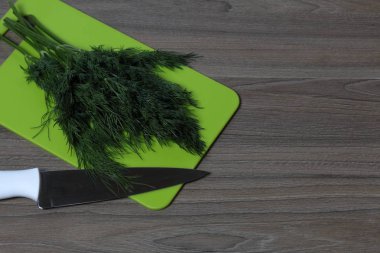 Taze yeşillikler düzgünce masanın üzerine serilir. Kokulu dereotu. Mutfak bıçağı ve kesme tahtasının yanında. Sağlıklı salata için Malzemeler.