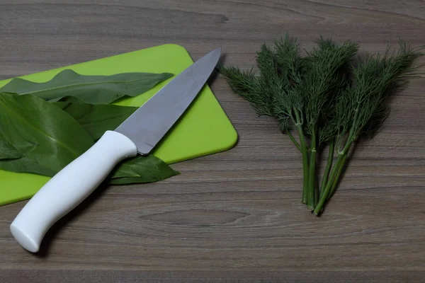 Verduras frescas cuidadosamente colocadas en la mesa. Ajo silvestre fragante y dil. Junto al cuchillo de cocina y la tabla de cortar. Ingredientes para ensalada saludable . — Foto de Stock