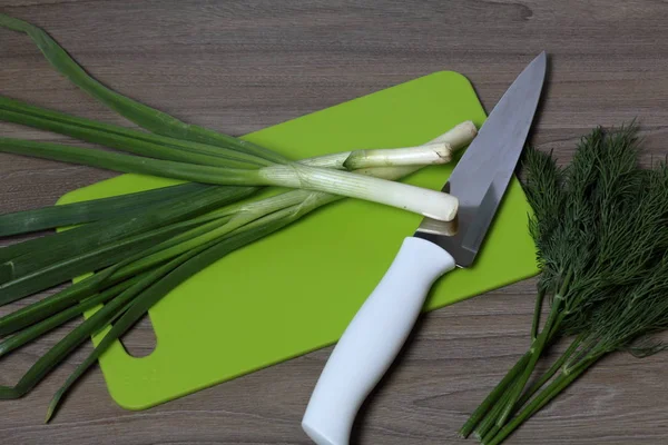 Verduras frescas cuidadosamente colocadas en la mesa. Cebollas aromáticas y eneldo. Junto al cuchillo de cocina y la tabla de cortar. Ingredientes para ensalada saludable . — Foto de Stock