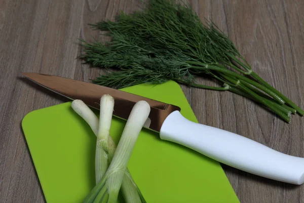 Verduras frescas cuidadosamente colocadas en la mesa. Cebollas aromáticas y eneldo. Junto al cuchillo de cocina y la tabla de cortar. Ingredientes para ensalada saludable . — Foto de Stock