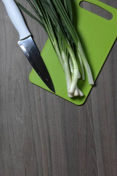 Fresh greens neatly laid out on the tabletop. Fragrant onions. Next to the kitchen knife and cutting board. Ingredients for healthy salad.