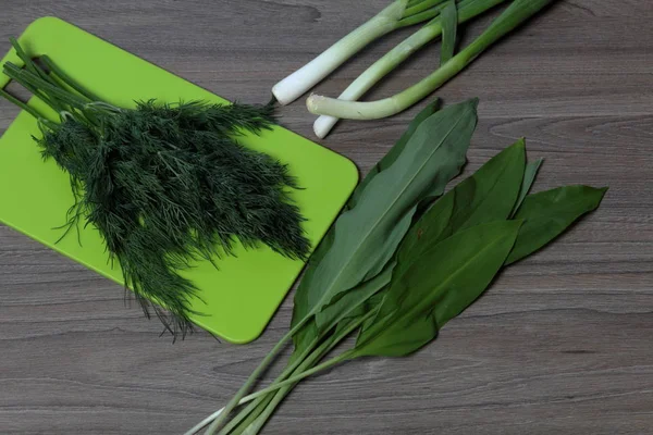 新鲜的绿色整齐地摆放在桌面上。洋葱、萝卜和野生大蒜。切割板旁边。健康沙拉的配料. — 图库照片