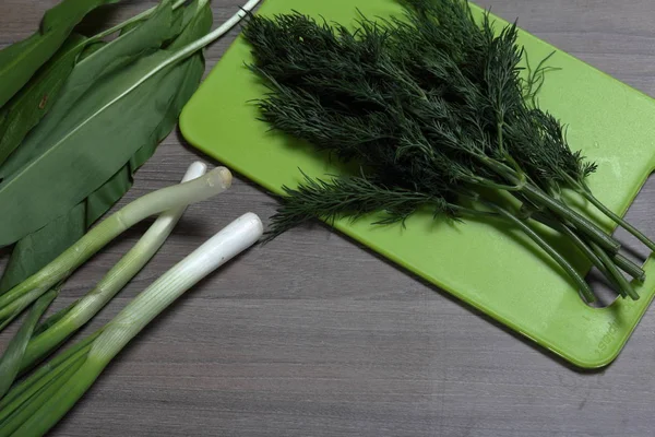 Verduras frescas cuidadosamente colocadas en la mesa. Cebollas aromáticas, eneldo y ajo silvestre. Junto a la tabla de cortar. Ingredientes para ensalada saludable . — Foto de Stock