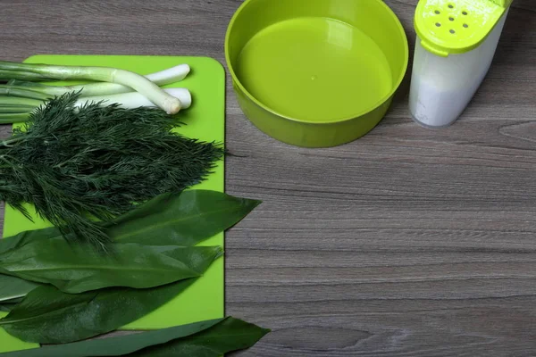 Verduras frescas cuidadosamente colocadas en la mesa. Cebollas aromáticas, eneldo y ajo silvestre. Cerca del contenedor para ensalada, salero y tabla de cortar . — Foto de Stock