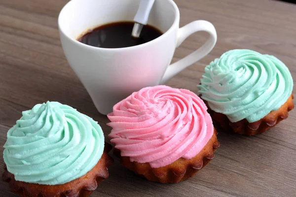 Trois gâteaux crème de différentes couleurs et une tasse de café. Une cuillère à café est déposée dans la tasse à café . — Photo