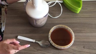 Bir kadın blender kabının kapağını kapatır ve helva yapmak için yer fıstığı ve tohum öğütür. Kabın yanında karışıma eklenecek bal var..