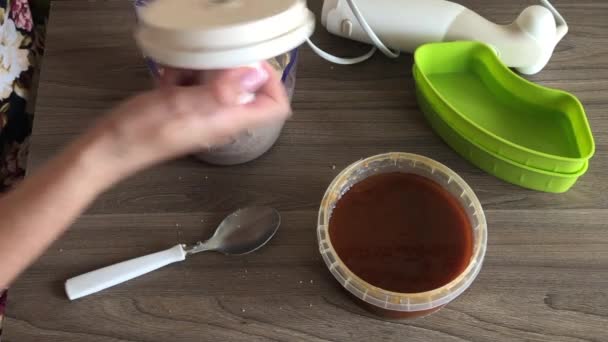 一个女人取下搅拌机的盖子 用勺子切碎的花生和种子混合 制作半白 容器旁边是蜂蜜添加到混合物 — 图库视频影像