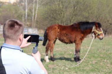 Akıllı telefondan videoya kaydolan genç bir adam. Düzgün çekim ler elde etmek için gimbal kullanır. Ekrana dokunarak kaydı kontrol eder.