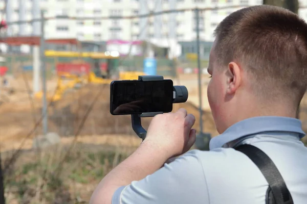 Un joven grabando en un smartphone. Utiliza gimbal para obtener imágenes suaves. Ver de cerca el rodaje de la película . — Foto de Stock