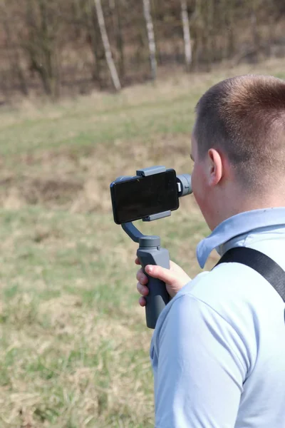 Ein junger Mann filmt mit seinem Smartphone. verwendet Gimbal, um reibungsloses Filmmaterial zu erhalten. Aufmerksam beim Filmdreh. — Stockfoto