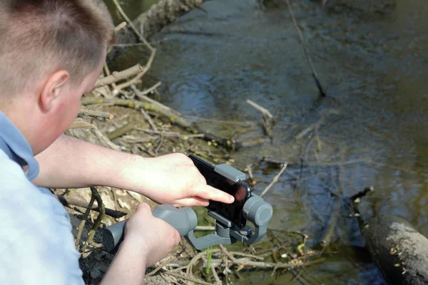 Ein junger Mann filmt mit seinem Smartphone. verwendet Gimbal, um glatte Aufnahmen zu erhalten. Steuerung der Aufnahme durch Berührung des Bildschirms. — Stockfoto