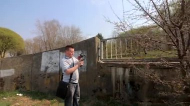 Genç bir adam spring parkta bir akıllı telefon video çekiyor. Elektronik gimbal kullanarak pürüzsüz çerçeveler için.
