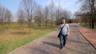 Genç bir adam spring parkta bir akıllı telefon video çekiyor. Elektronik gimbal kullanarak pürüzsüz çerçeveler için.
