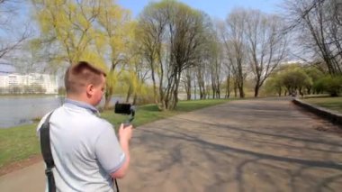 Genç bir adam spring parkta bir akıllı telefon video çekiyor. Elektronik gimbal kullanarak pürüzsüz çerçeveler için.