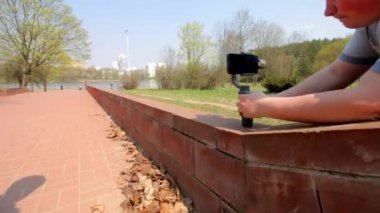 Bahar parkında patika. Fayanslarla döşenmiş. Genç bir adam elektronik bir gimbal kullanarak bir akıllı telefon video çekimleri..