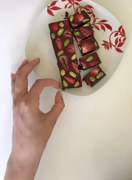 A woman takes homemade chocolate with dried strawberries and pistachios from a plate. — Stock Photo, Image