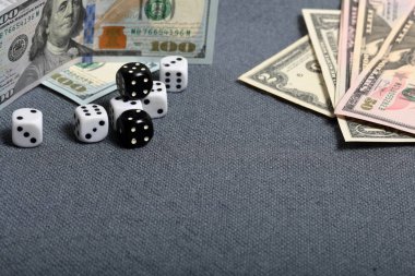 Siyah işaretli beyaz zarlar. Kaba gri bir bezle kaplı bir yüzeye uzanıyorlar. Aralarında beyaz işaretli iki siyah zar var. Yakınlarda birkaç dolarlık banknotlar var..