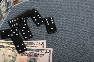 Kaba gri bir bezle kaplı bir yüzeyde domino eklemleri. Yakında farklı mezheplerden birkaç dolarlık banknotlar var..