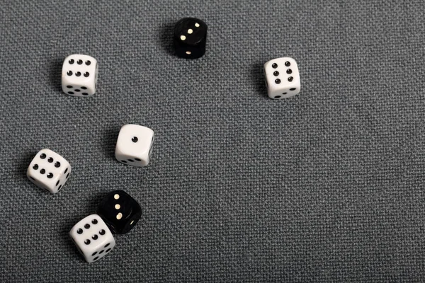 Білі кубики з чорними позначками. Вони лежать на поверхні, покритій грубою сірою тканиною. Серед них два чорні кубики з білими розмітками . — стокове фото