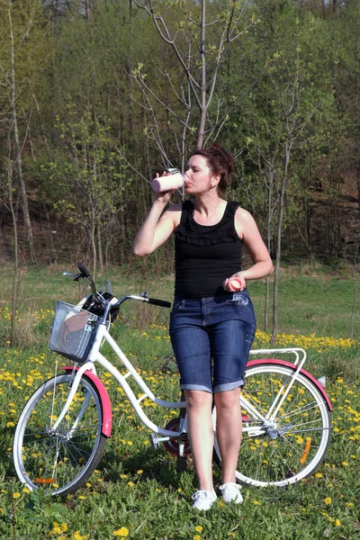 Das Mädchen stützt sich auf ein geparktes Fahrrad. Ruhe auf den Frühlingszyklus. das Mädchen trinkt Wasser aus einer Flasche. — Stockfoto