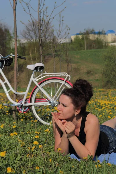 La fille repose sur la prairie printanière. Allongé sur le couvre-lit. A proximité se trouve un vélo. Les pissenlits fleurissent, les jeunes herbes poussent . — Photo