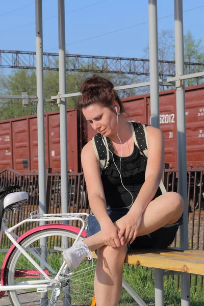 Ein Mädchen sitzt auf einer Bank und hört Musik. In der Nähe liegt ihr Fahrrad. — Stockfoto