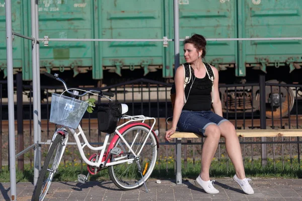 Девушка сидит на скамейке и слушает музыку. Рядом ее велосипед. . — стоковое фото