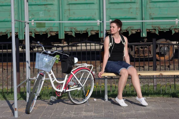 Ein Mädchen sitzt auf einer Bank und hört Musik. In der Nähe liegt ihr Fahrrad. — Stockfoto