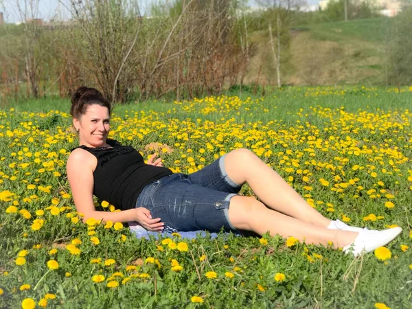 Das Mädchen ruht sich auf der Frühlingswiese aus. liegt auf der Bettdecke. Löwenzahn blüht, junges Gras wächst. — Stockfoto