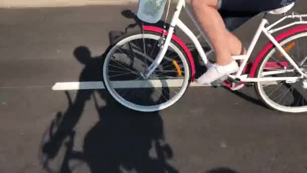 女の子はアスファルトの道で自転車に乗ります 貨物バスケットの中に花束 — ストック動画