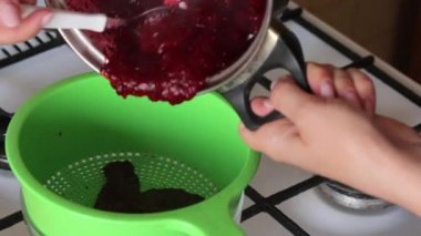 Bir kadın şekerle pişirilen kızılcıkları bir tencereden kevgire aktarıyor. Marshmallow için patates püresi hazırlar.