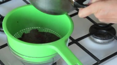 Bir kadın şekerle pişirilen kızılcıkları bir tencereden kevgire aktarıyor. Marshmallow için patates püresi hazırlar.