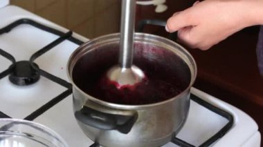 Blender kullanan bir kadın şeker ve donmuş kızılcıkları bir tencerede eziyor. Marshmallow için patates püresi hazırlar.