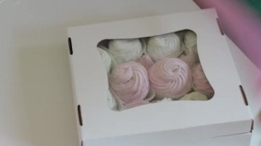 Bir kadın bir kutu şekerleme çalıyor. Kutudaki saydam pencereden görülebilen farklı renklerde marshmallow.