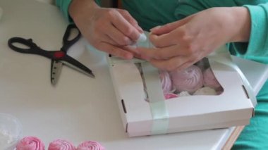 Bir kadın bir kutu şekerleme çalıyor. Bir yay bağlar. Kutudaki saydam pencereden görülebilen farklı renklerde marshmallow..