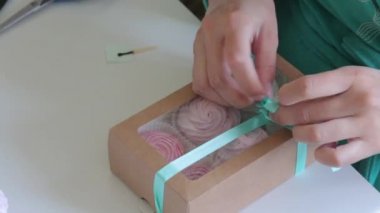 Bir kadın ev yapımı şekerlemelerle bir kutuya kurdele yayı bağlar. Hediye kutusunda farklı renk marshmallows.