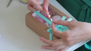 Hediye kutusunda farklı renklerde ev yapımı marshmallow. Bir kadın bir örgü ile bir kutu bağlı, bir yay bağlı ve bir maç ile kurdele nin biter cauterized.