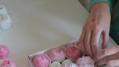Kadın marşmelovu hediye kutusuna koyuyor. Şekerlemeler farklı renklerde, masanın yüzeyine serilmiş..
