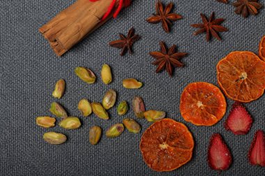 Kurutulmuş mandalina ve çilek, tatlı süslemek için parçalarhalinde kesilmiş. Yakınlarda antep fıstığı, anason ve kırmızı iplikle bağlanmış tarçın çubukları bulunmaktadır. Gri arka planda.