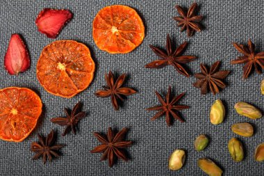 Kurutulmuş mandalina ve çilek, tatlı süslemek için parçalarhalinde kesilmiş. Otelin yakınında antep fıstığı ve anason bulunmaktadır. Gri arka planda.