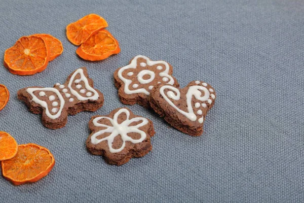 Galletas de jengibre decoradas con un patrón de esmalte blanco. Sobre un fondo de tela gris. Decorado con elementos decorativos de frutos secos — Foto de Stock